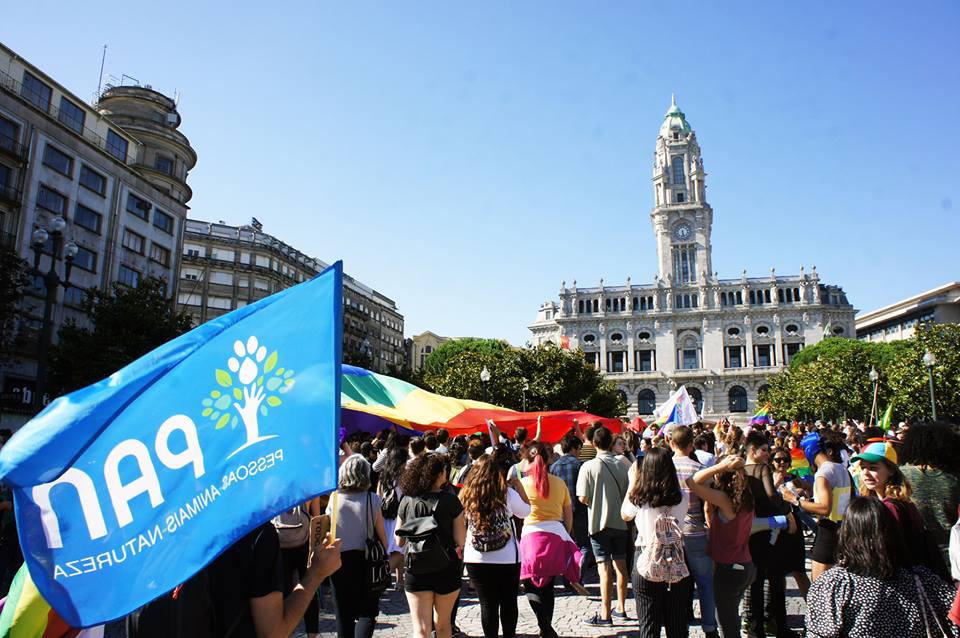 Na imagem podemos ver uma bandeira do PAN e uma grande bandeira arco-íris na Praça dos Aliados, cidade do Porto